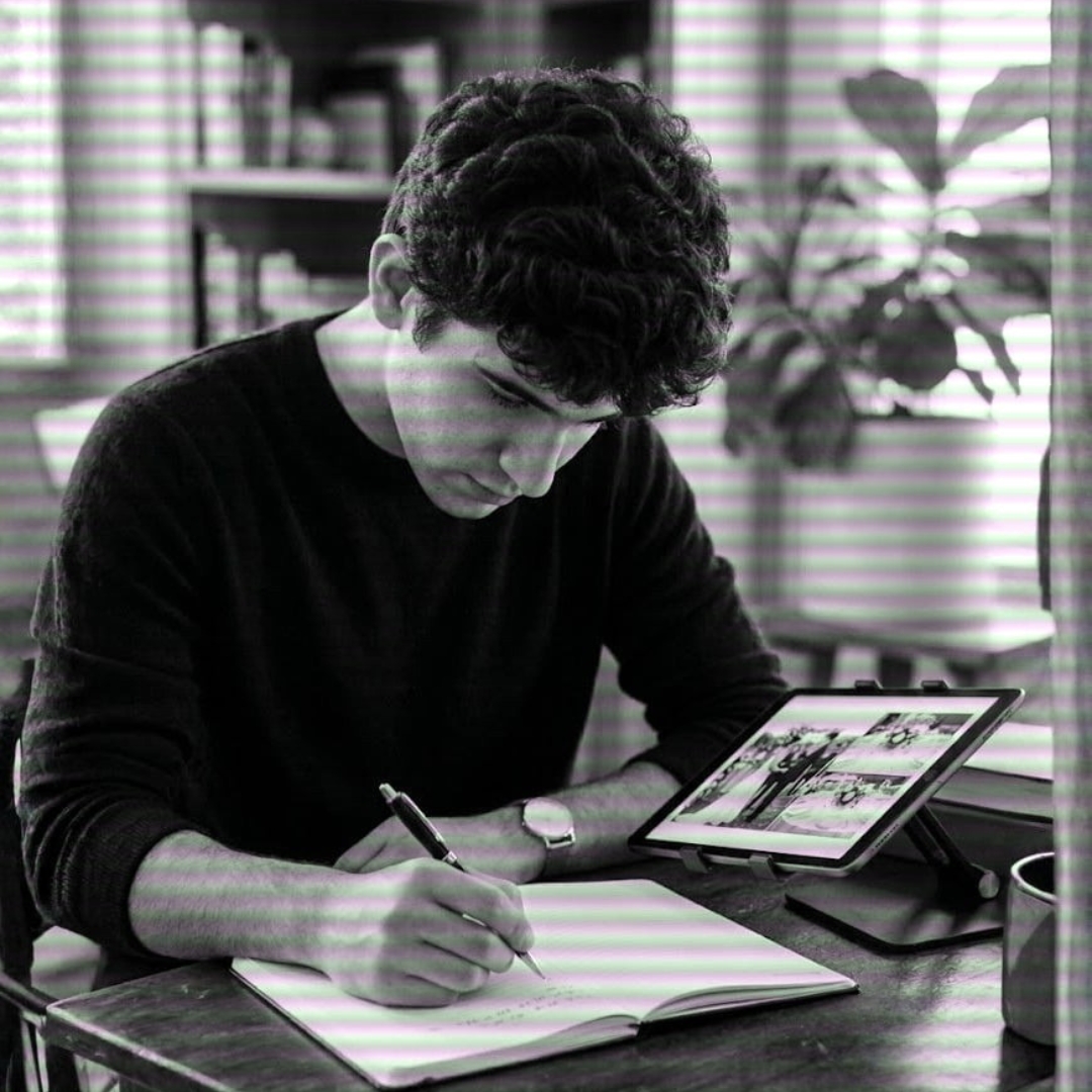 Juan sketching in a notebook with a tablet showing wedding photos in the background